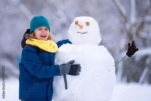 Kid play with snowman in winter. Snowman with a carrot nose on a winters day. Child making snowman. Little boy building snowball for funny snowman in snowy winter park. Snowmen in a snowy winter park.