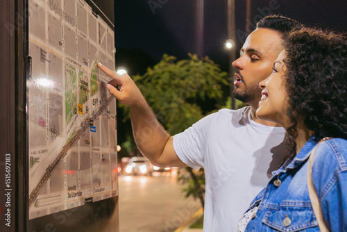 Young Latin couple looks at a city map with street names in spanish, lost in the city at night