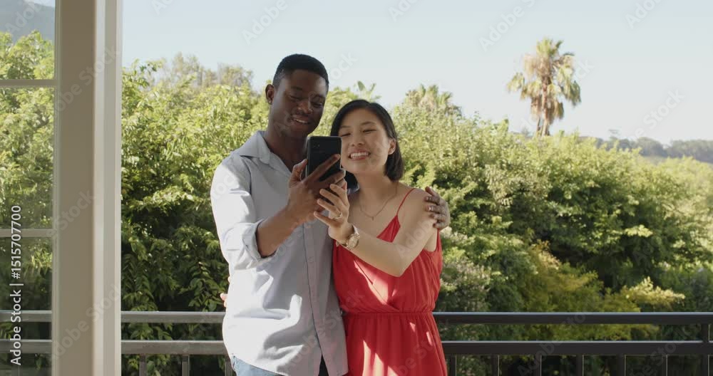 Diverse couple stepping onto balcony, recording smartphone call greeting friend showing green view