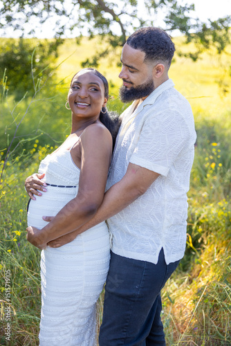 A loving African American couple is sharing a beautiful and joyful moment outdoors, as they celebrate the exciting news of their pregnancy under the warm and bright sunshine of summer
