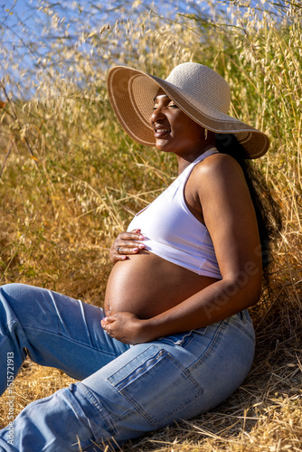 A serene pregnant woman enjoys a peaceful moment in nature, proudly highlighting her beautiful baby bump. The warm summer light enhances the joy of pregnancy and her deep connection with the outdoors