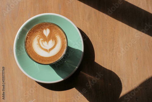 Latte art in a cup on a wooden surface with sunlight and shadow.