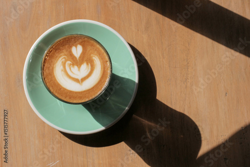 Latte art in a cup on a wooden surface with sunlight and shadow.