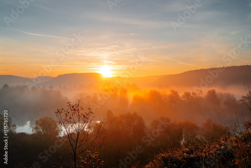 Orange picturesque sunrise over the river with morning mists.