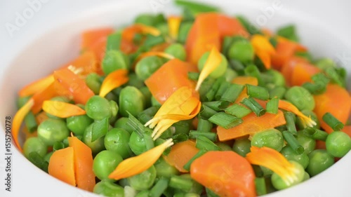 Fresh garden peas and carrots are cooked with salted butter, then garnished with chives and bright marigold flowers for an appealing and colorful side dish.