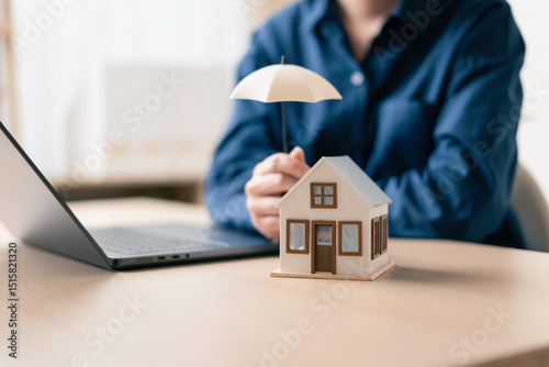 insurance agent presenting a small house under an umbrella on a desk with a laptop to demonstrate virtual home insurance quotes and coverage options