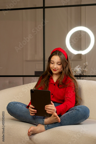 Teen girl sitting cross-legged on sofa using tablet device. Concept of lifestyle, use digital technology