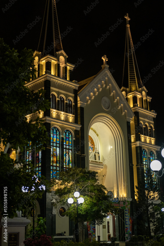 Obraz premium The Catholic Church Cathedral at night, illuminated by warm yellow light. Serene and picturesque view of the landmark. View of Ba Lang Church, Nha Trang city Vietnam. Travel photo. 