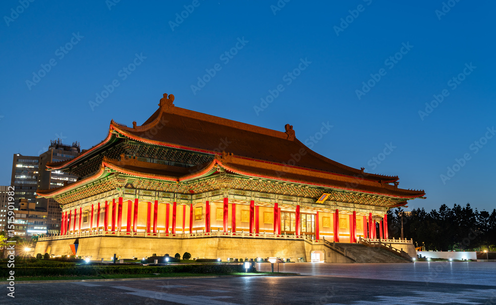 Obraz premium The National Theater in Taipei, Taiwan glows under evening lights, its vibrant red columns and ornate roof standing out against a deep blue sky in Liberty Square