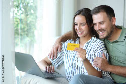 Happy couple buying online using card and laptop in a house