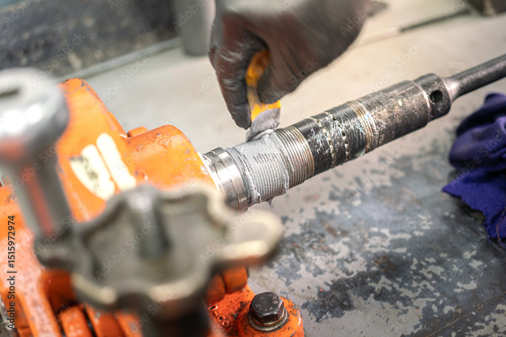 Ταπετσαρία A serviceman is lube lubricant or thread protection chemical on the equipment's thread which is gripping on the metal workbench
