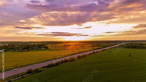 Sunset over A3 Highway. An aerial view captures a highway in Gherghița, Prahova County, Romania, bathed in the warm, golden light of sunset. The sun, low on the horizon, casts a glow over the road.