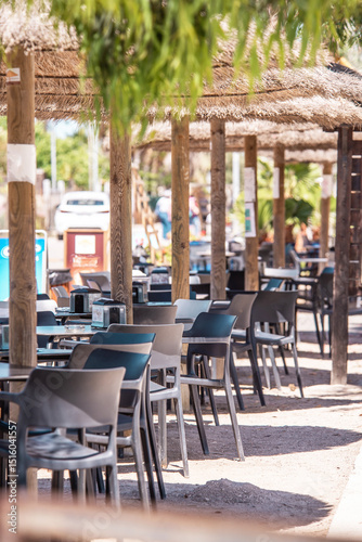 Tropical restaurant with plastic chairs and straw umbrellas on a shaded terrace near the road. Vacation in an exotic hot country. Restaurant business. Economic Crisis. Empty cafe