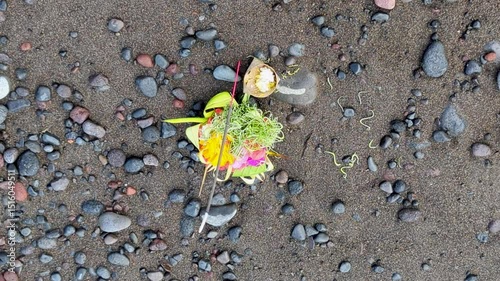 Top down of Balinese Hindu canang sari offering to gods and spirits with food, flowers, and smoking incense stick on beach on tropical island of Bali Indonesia photo