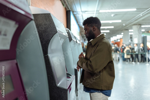 Young man buying train ticket at automatic machine in subway station