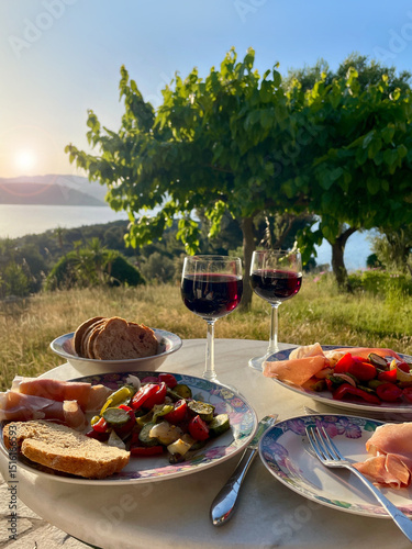 mediterranean dinner outdoor with a view to the garden and the sea in sunset with red wine