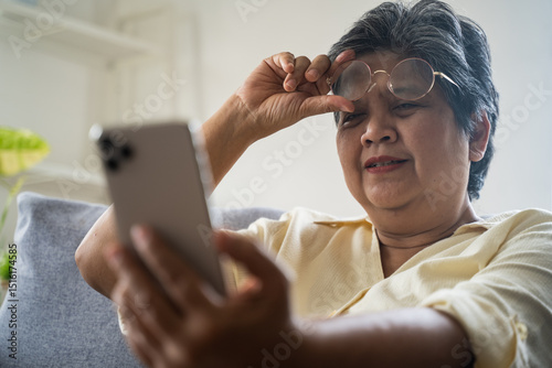 Asian senior fatigue woman taking off eye glasses during using smartphone after surfing internet or social media at home. Elderly retired male eyesight problem or blurry vision from old aged