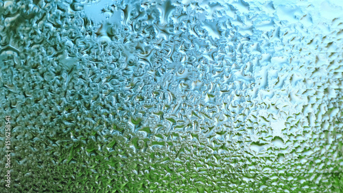 Water Drops on a glass. Dripping rain drops textured background. Close up of misted window with droplets draining down. Increased air humidity. Rainy weather. Blue green colors. High quality photo.