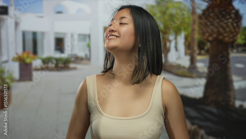 Young woman on city street smiling contently as she takes a deep breath, showing calm and serenity in an urban outdoor setting with trees and white buildings in the background. Free Download Young woman on city street smiling contently as she takes a deep breath, showing calm and serenity in an urban outdoor setting with trees and white buildings in the background. - GFXLoad