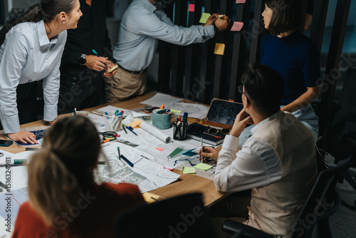 A multicultural team of business colleagues discuss and brainstorm innovative project solutions. Working late, they focus on meeting a critical deadline with collaborative energy and creative ideas. photo