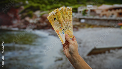 Wallpaper Mural Hand holding philippine pesos outdoors by the seaside, depicting investment and business themes in a scenic town setting. Torontodigital.ca