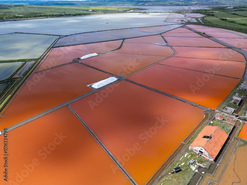 Aerial view of colorful salt pans near Burgas, Bulgaria. Vibrant red and orange evaporation ponds contrast with white salt piles and turquoise sea. Industrial and natural beauty combined
