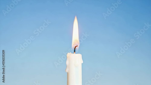 White candle burning with flame against clear blue sky  