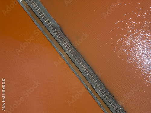 Aerial view of colorful salt pans near Burgas, Bulgaria. Vibrant red and orange evaporation ponds contrast with white salt piles and turquoise sea. Industrial and natural beauty combined