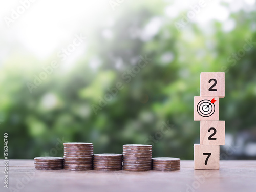 Wooden blocks with the number 2027 and stack of coins. The concept of saving money, Financial, Investment and Business growing in year 2027.