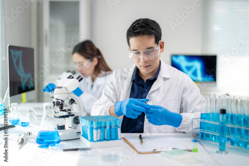 A man in a lab coat is wearing gloves and looking at a computer monitor