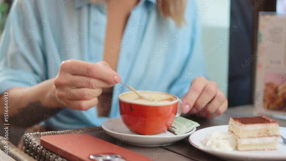 Young woman enjoy relaxing moment at cafe, stirring cappuccino with teaspoon before taking sip, delicious piece of cake awaits on side