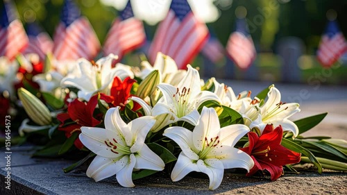White and red lilies rest on a stone surface with american flags waving gently in the background.