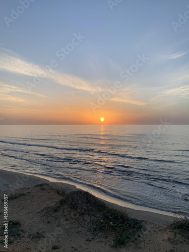 Sunset over calm ocean waves at sandy beach shore  