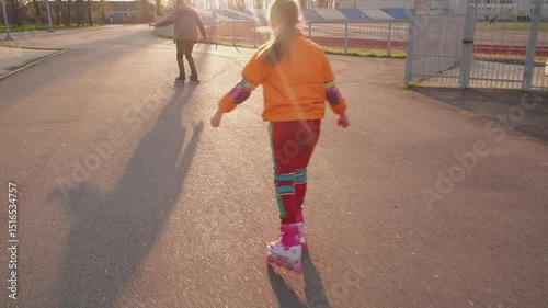 Low-angle view captures a child's vibrant rollerblading adventure on grey asphalt. Brightly colored clothing and pink skates symbolize youthful energy and freedom of movement.