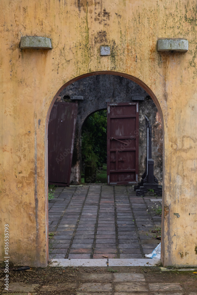 Fototapeta premium Open stone arch against the background of abandoned ancient buildings and antique ruins. In the background, broken door leaves. A mystical setting