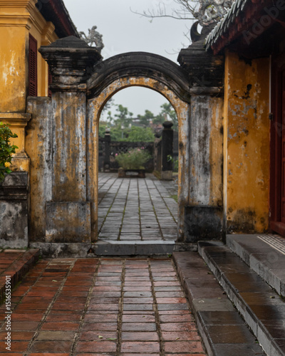 Open stone arch against the background of abandoned ancient buildings and antique ruins. In the background, broken door leaves. A mystical setting