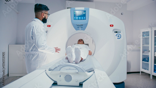 Obraz na plátně Bearded technician wearing lab coat turning control knob while medical bed carrying female patient sliding inside MRI tunnel