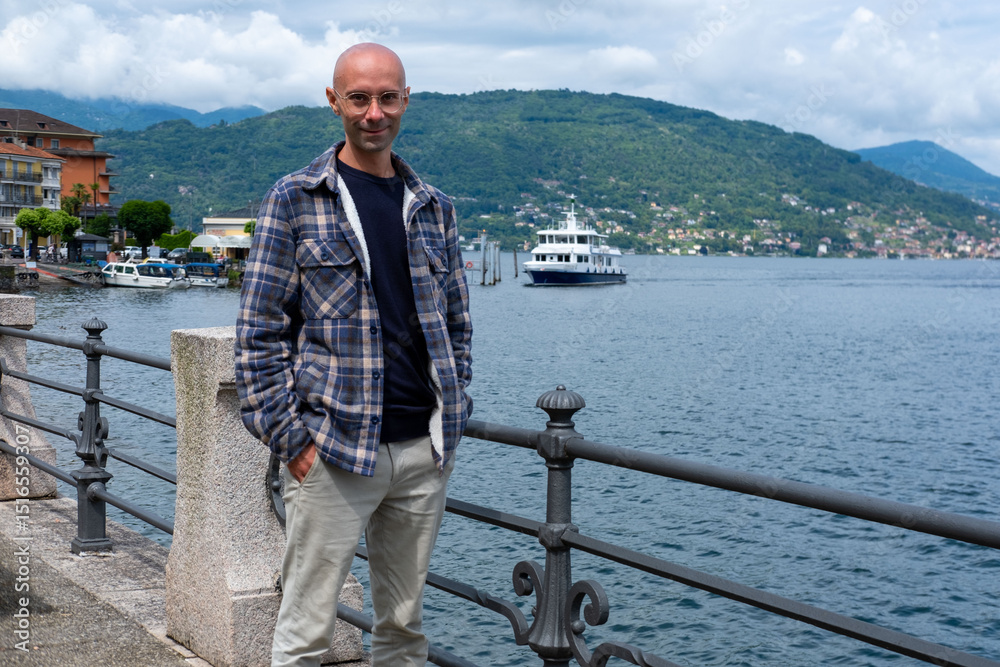 Obraz premium Young traveler man relaxing on Baveno promenade, man enjoying Marjorie lake view, summer breeze, peaceful moment, solo trip, scenic destination