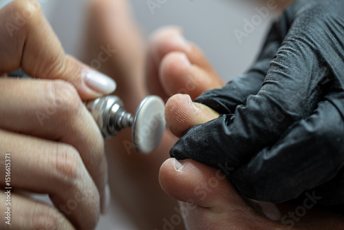 Close-up of professional manicurist using electric buffer tool on fingernail during nail care procedure photo