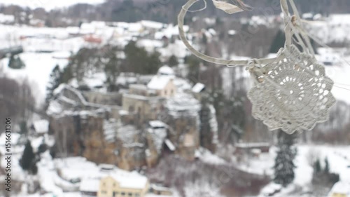 Handcrafted crocheted ornament hanging with a blurred view of a picturesque snowy village and tranquil winter scenery in the background
