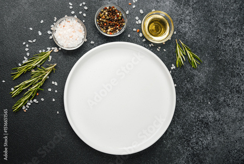 Empty white plate with herbs and spices on black stone background photo