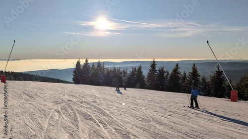Skiers slide across a snow-covered plain as the sun slowly sets in the background in winter