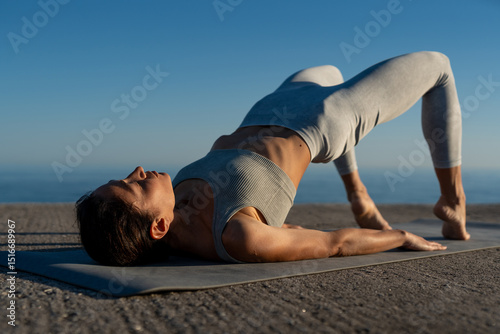 Focused woman practicing a single-leg bridge pose on a yoga mat during a peaceful outdoor session by the sea photo