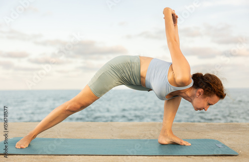 Example of performing hatha yoga asana. Amateur and professional girl doing yoga near sea, on embankment she fulfil elongated side angle, Utthita Parshvakonasana photo