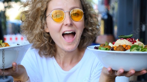 Foto Excited curly blonde haired woman wearing yellow sunglasses showing two bowls of