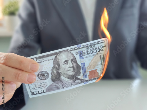 Money burning in a person's hand while wearing a suit with a blurred background