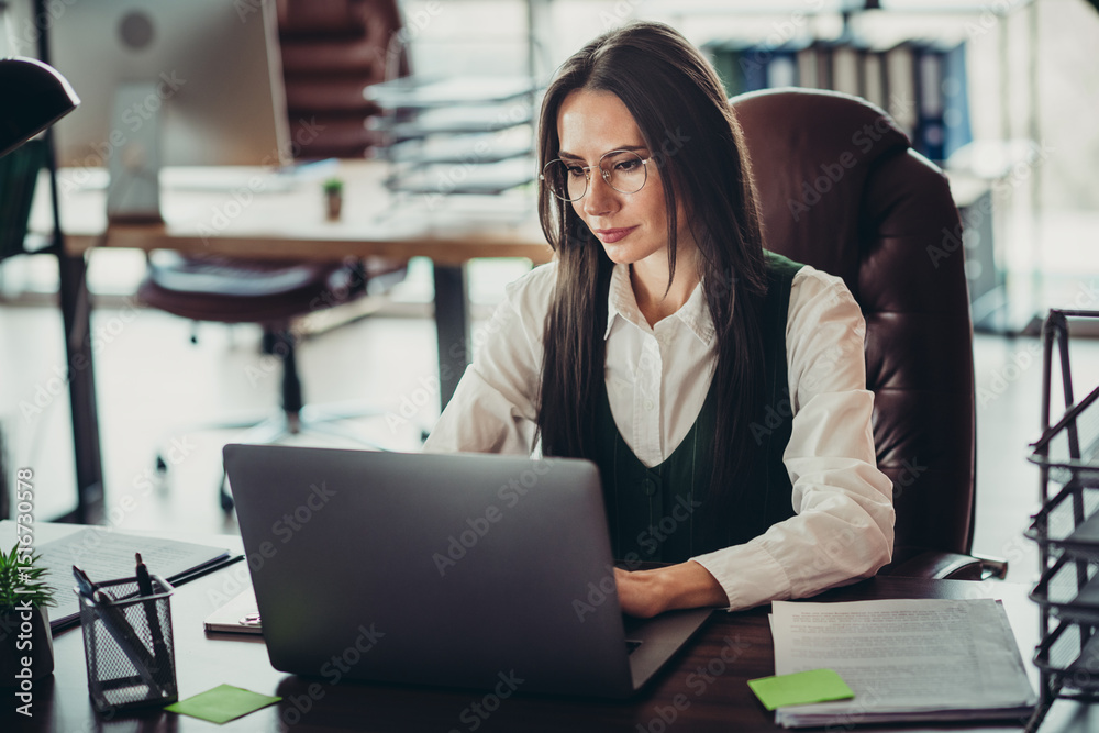 Obraz premium Confident businesswoman working on a laptop at her office desk, showcasing focus and professionalism in a corporate environment