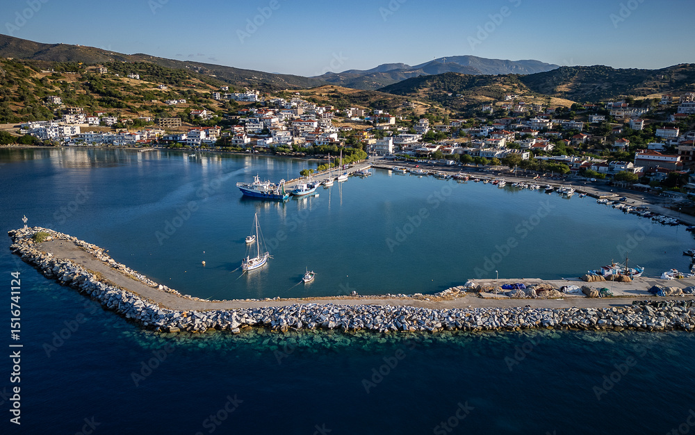 Naklejka premium Aerial view of Agii Apostoli, Greece – a serene coastal village with whitewashed houses, fishing boats, and deep blue waters framed by rolling hills and warm Mediterranean 
