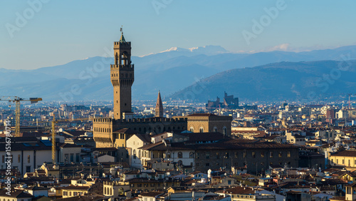 Panoramic view of Florence with Palazzo Vecchio and Torre di Arnolfo, Tuscany, Italy, framed by rooftops and snowy Apennine mountains.