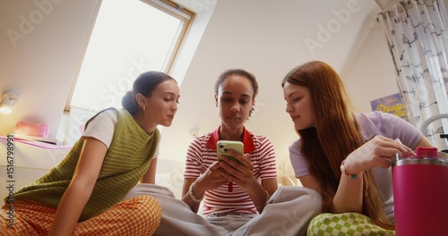 Foto Three teenage girls are using a mobile phone and talking